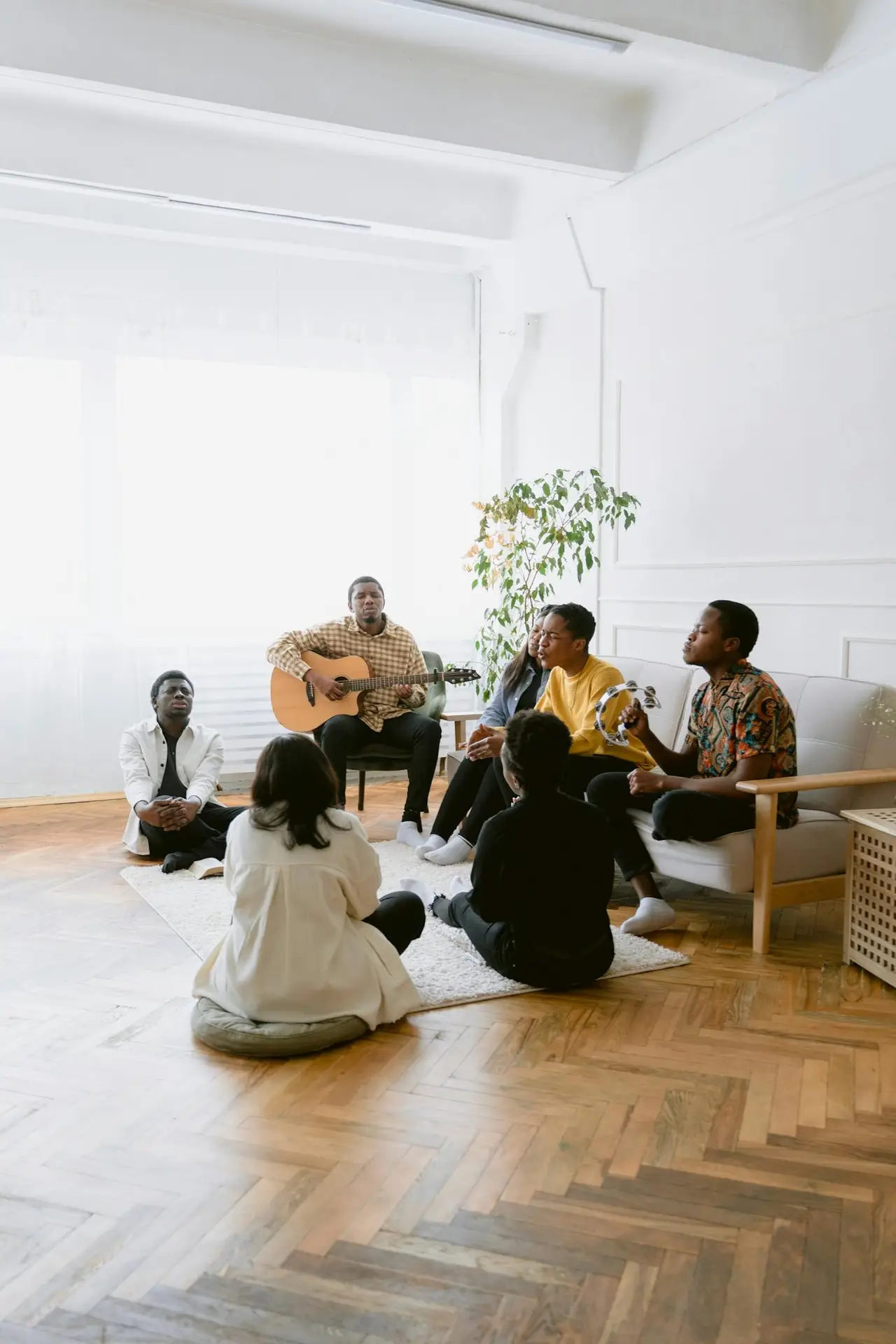 A diverse group of people praying and singing with a guitar in a cozy room setting, capturing a spiritual moment.