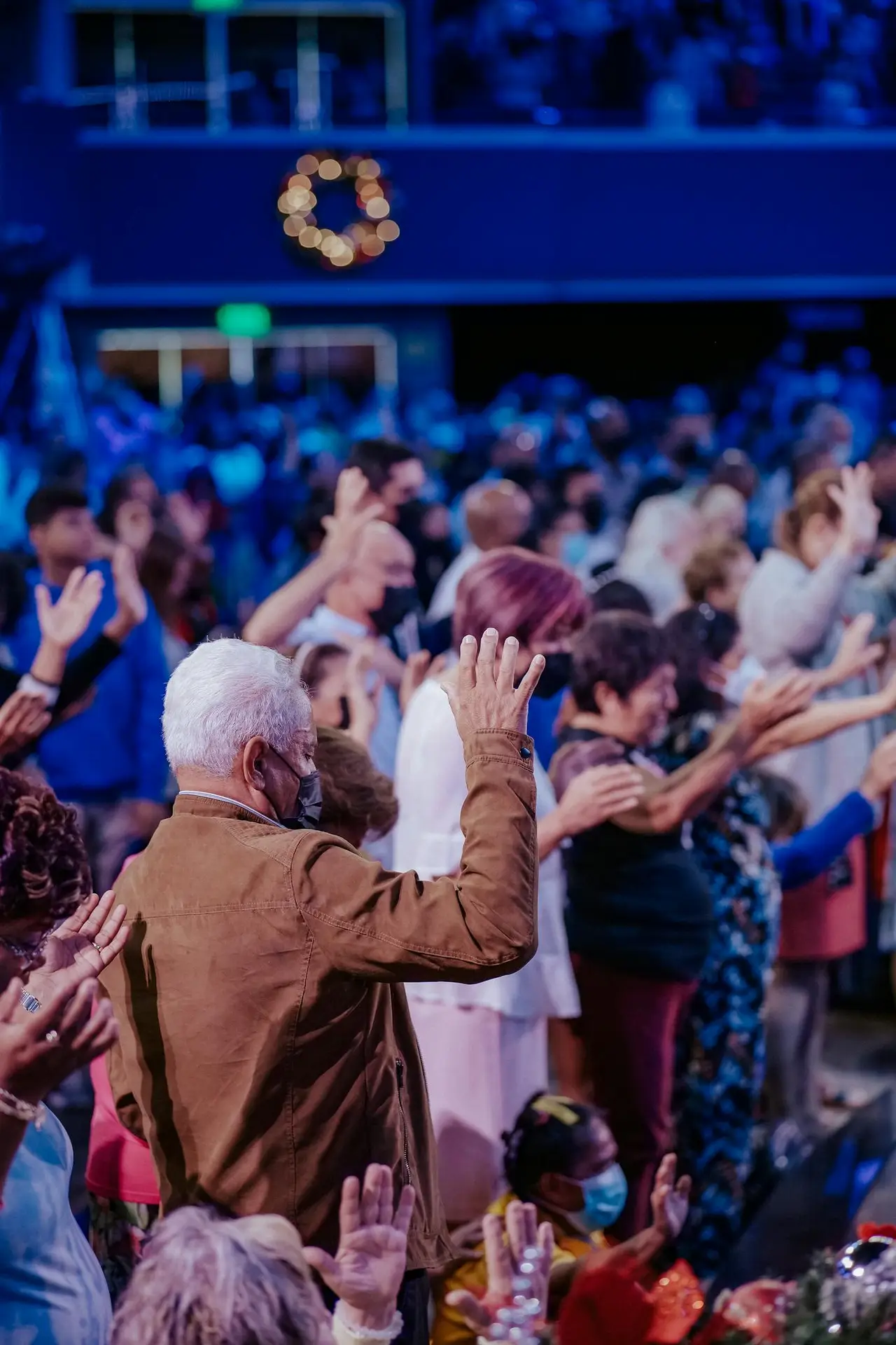 A vibrant crowd at an event, raising hands in unity under blue lighting, creating a joyous atmosphere.